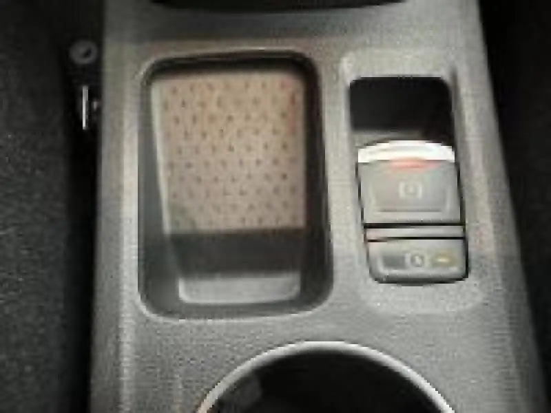 Gros plan sur la console centrale grise du Renault Captur 2025, avec bouton de frein à main électronique et rangement adjacent.