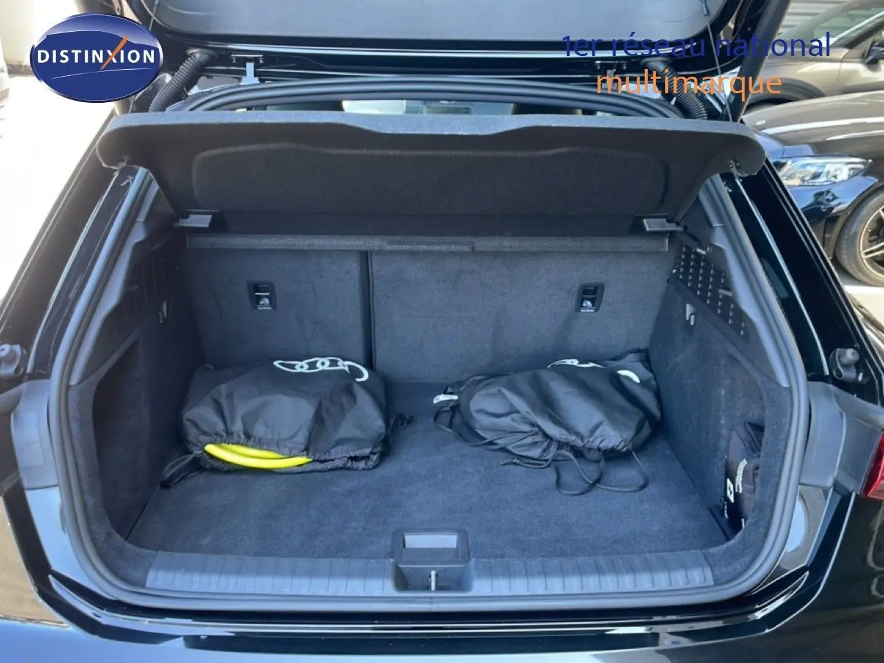 Coffre ouvert d’une Audi A3 Sportback noir mito metal, vue arrière montrant un espace de rangement avec deux sacs noirs.