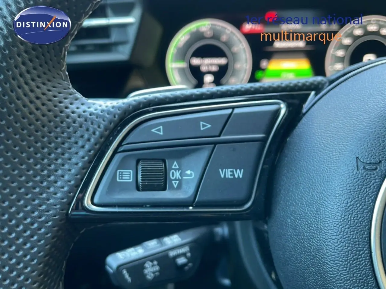 Gros plan sur les commandes à gauche du volant perforé noir de l'Audi A3 Sportback 40 TFSIe 2025 avec tableau de bord numérique flou.