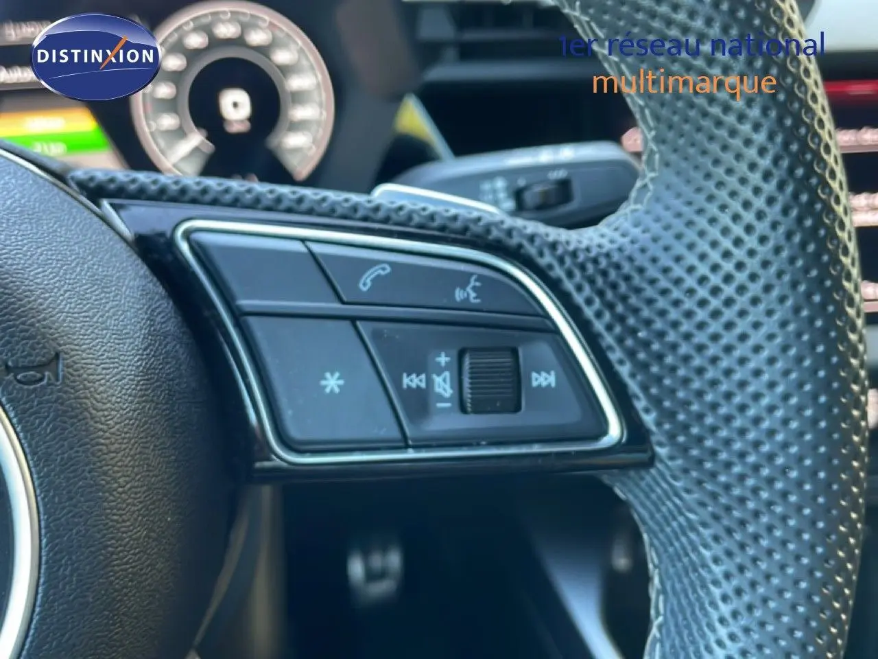 Gros plan sur le volant perforé de l'Audi A3 Sportback noir mito metal, avec commandes audio et téléphone intégrées.