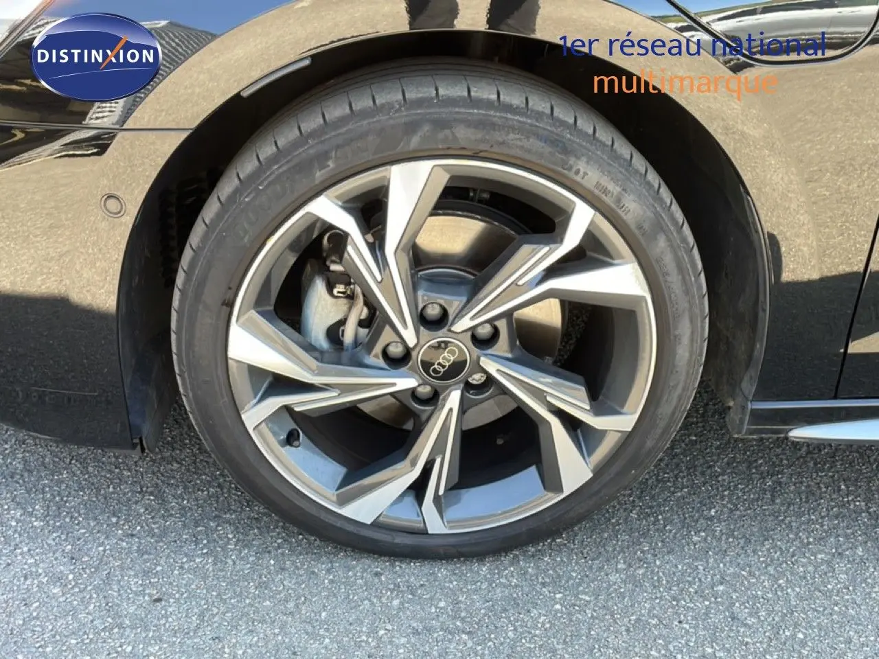 Gros plan sur la roue avant droite d’une Audi A3 Sportback noire, mettant en valeur la jante en alliage au design moderne.
