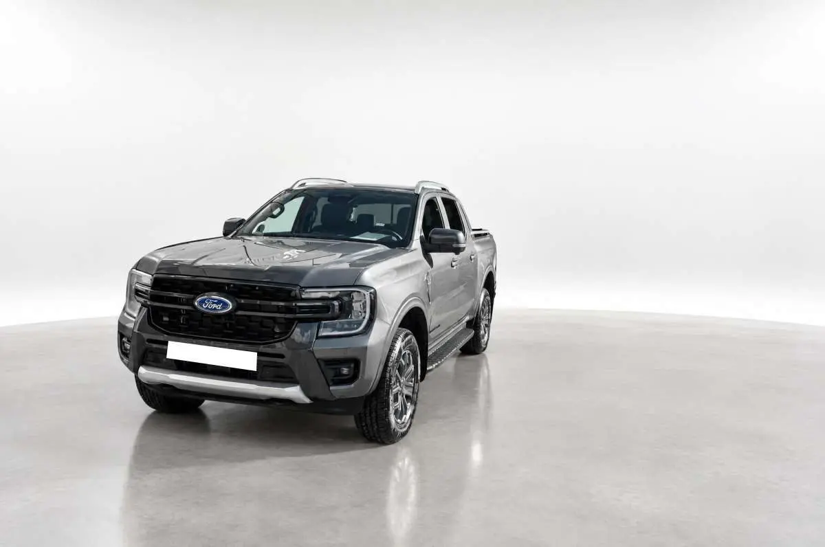 Ford Ranger 2.0 Wildtrak gris carbone en 3/4 avant droit, avec calandre noire et barres de toit visibles.