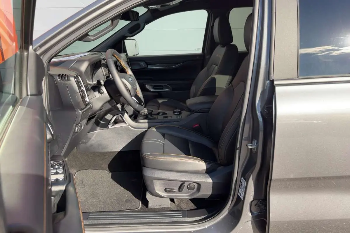 Vue intérieure côté conducteur du Ford Ranger gris carbone 2026, sièges en cuir avec surpiqûres orange et volant multifonctions.