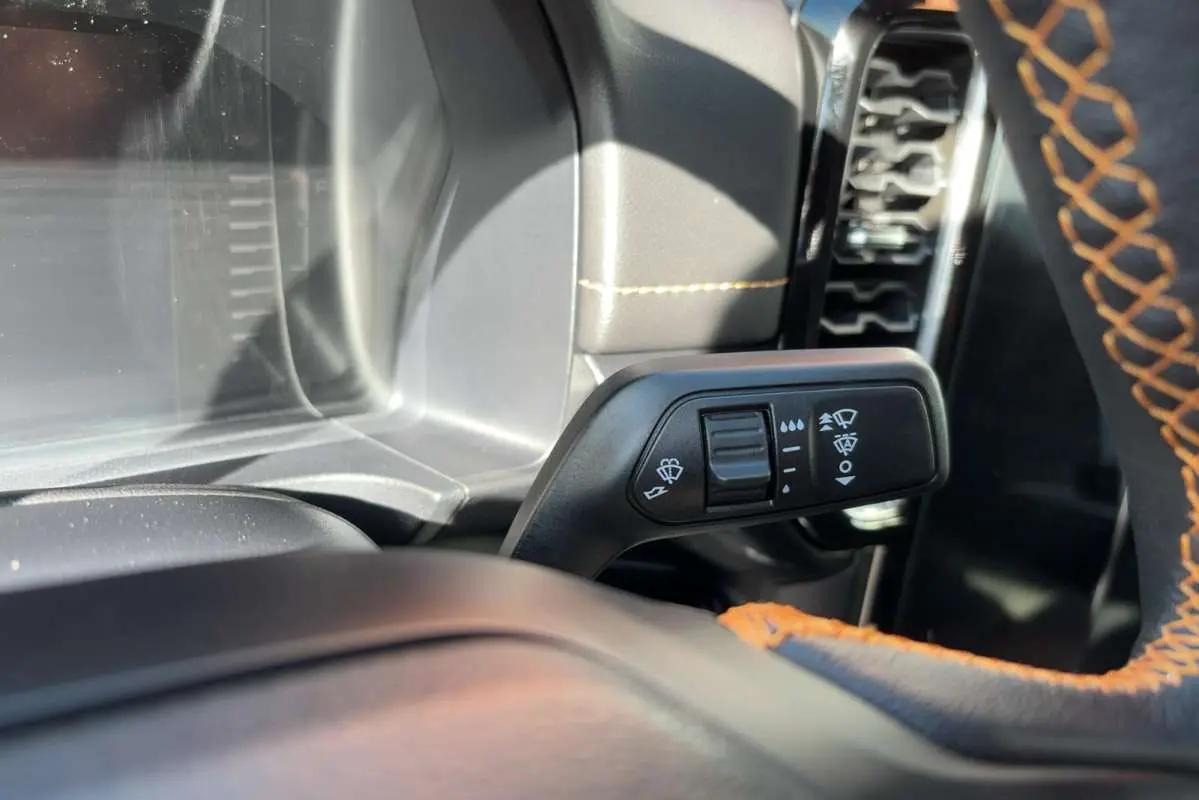 Gros plan sur la commande des essuie-glaces à gauche du volant cuir noir avec surpiqûres orange du Ford Ranger gris carbone.