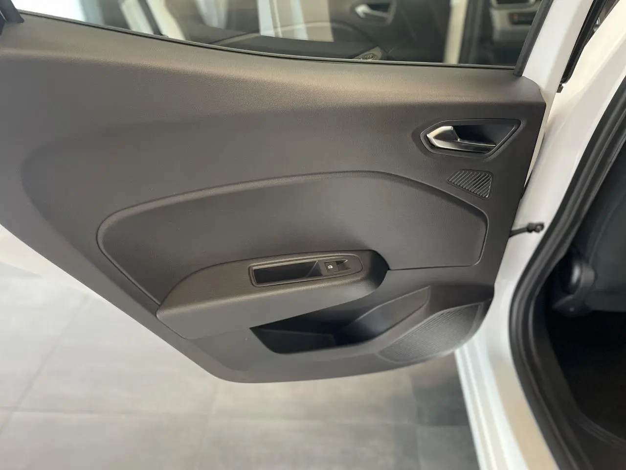Porte intérieure côté arrière droit de la Renault Clio blanche 2025 avec poignée et commande de vitre noire.