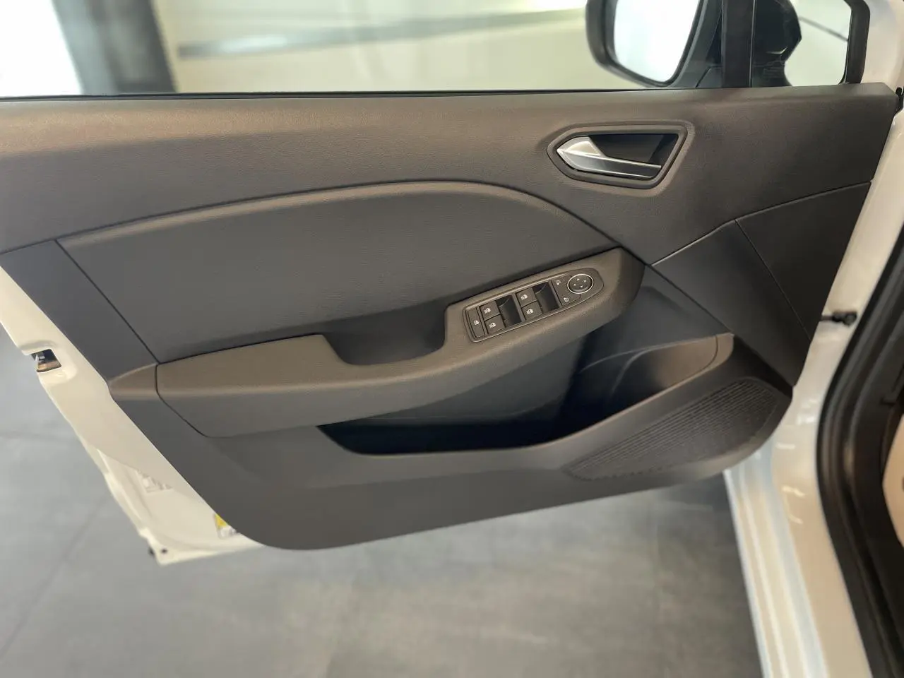 Vue intérieure de la porte avant gauche noire de la Renault Clio blanche avec commandes de vitres et rétroviseurs électriques.