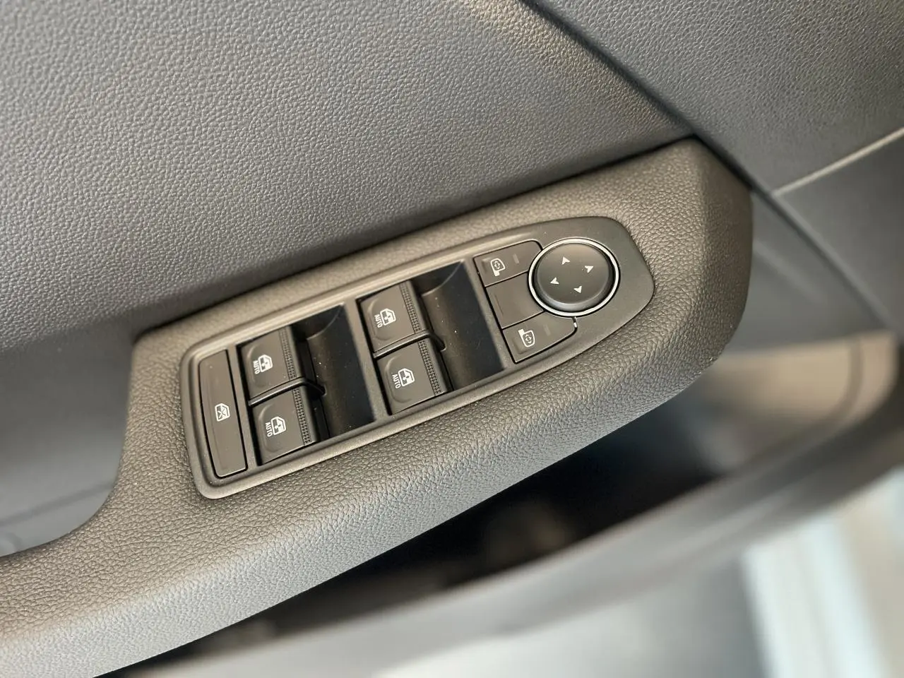 Gros plan sur les commandes des vitres électriques et rétroviseurs côté conducteur d'une Renault Clio blanche 2025.
