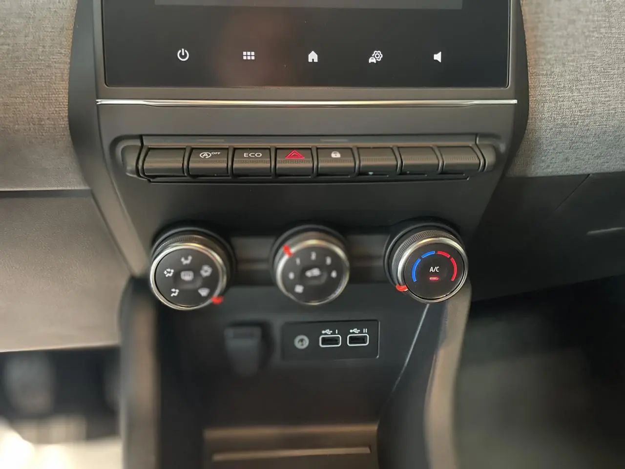Gros plan sur la console centrale de la Renault Clio 2025 avec commandes de climatisation et ports USB visibles.