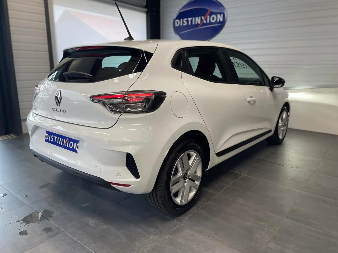 Vue 3/4 arrière droite d'une Renault Clio blanche Glacier avec feux arrière LED et jantes alliage en intérieur showroom.