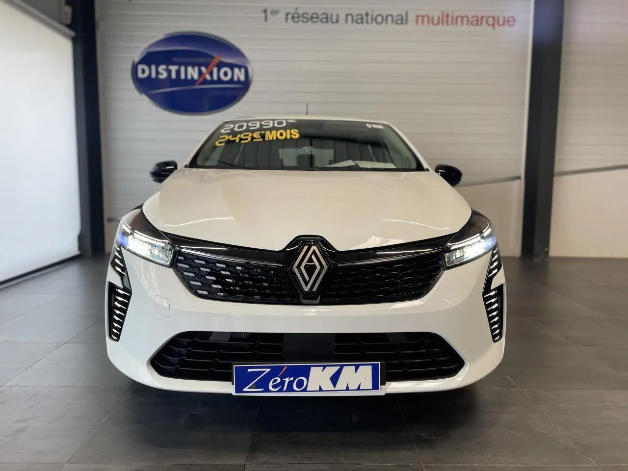 Vue frontale d'une Renault Clio blanche 2025 avec calandre noire et feux LED allumés en showroom.
