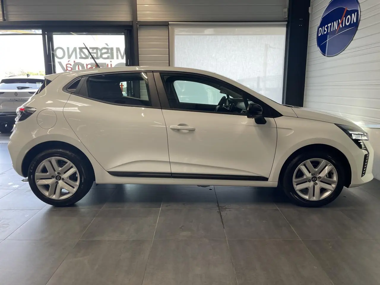 Profil droit d'une Renault Clio blanche 2025 avec jantes alliage et poignées couleur carrosserie en showroom.
