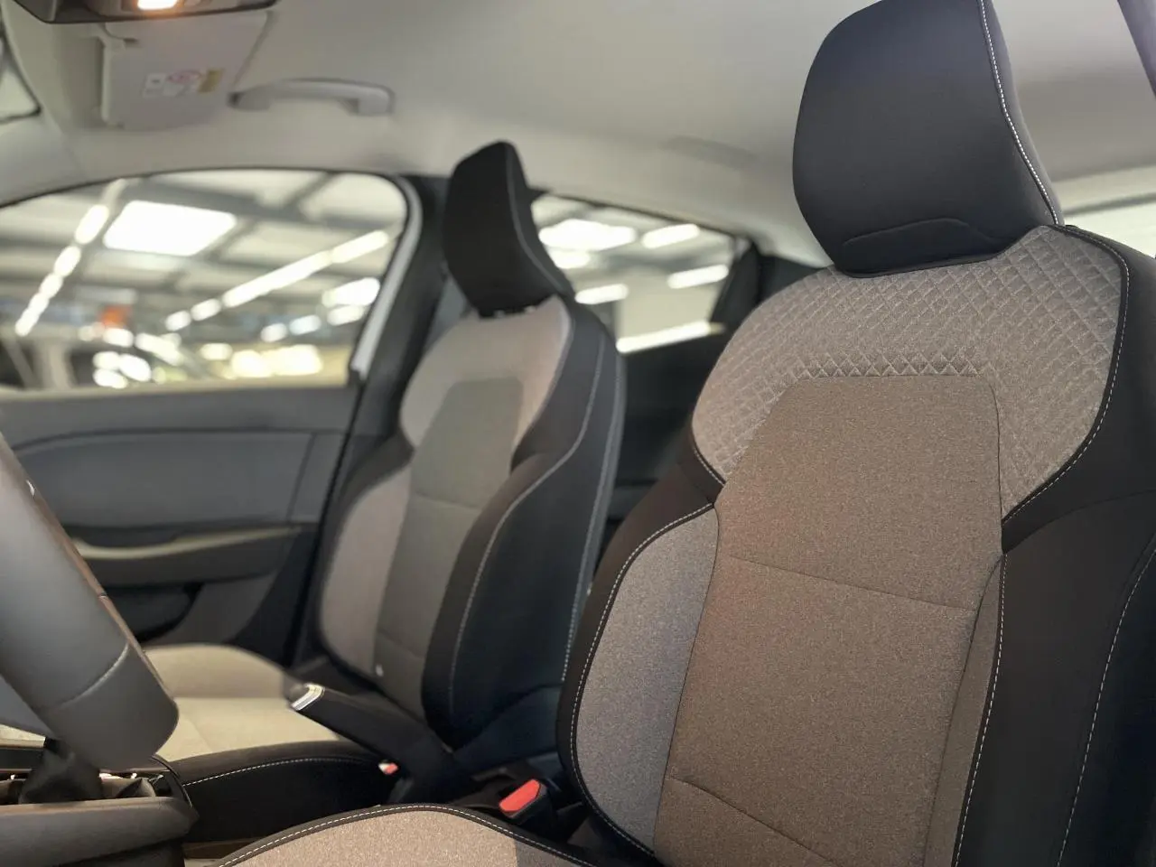 Vue intérieure rapprochée des sièges avant gris et noirs de la Renault Clio 2025 avec coutures blanches apparentes.