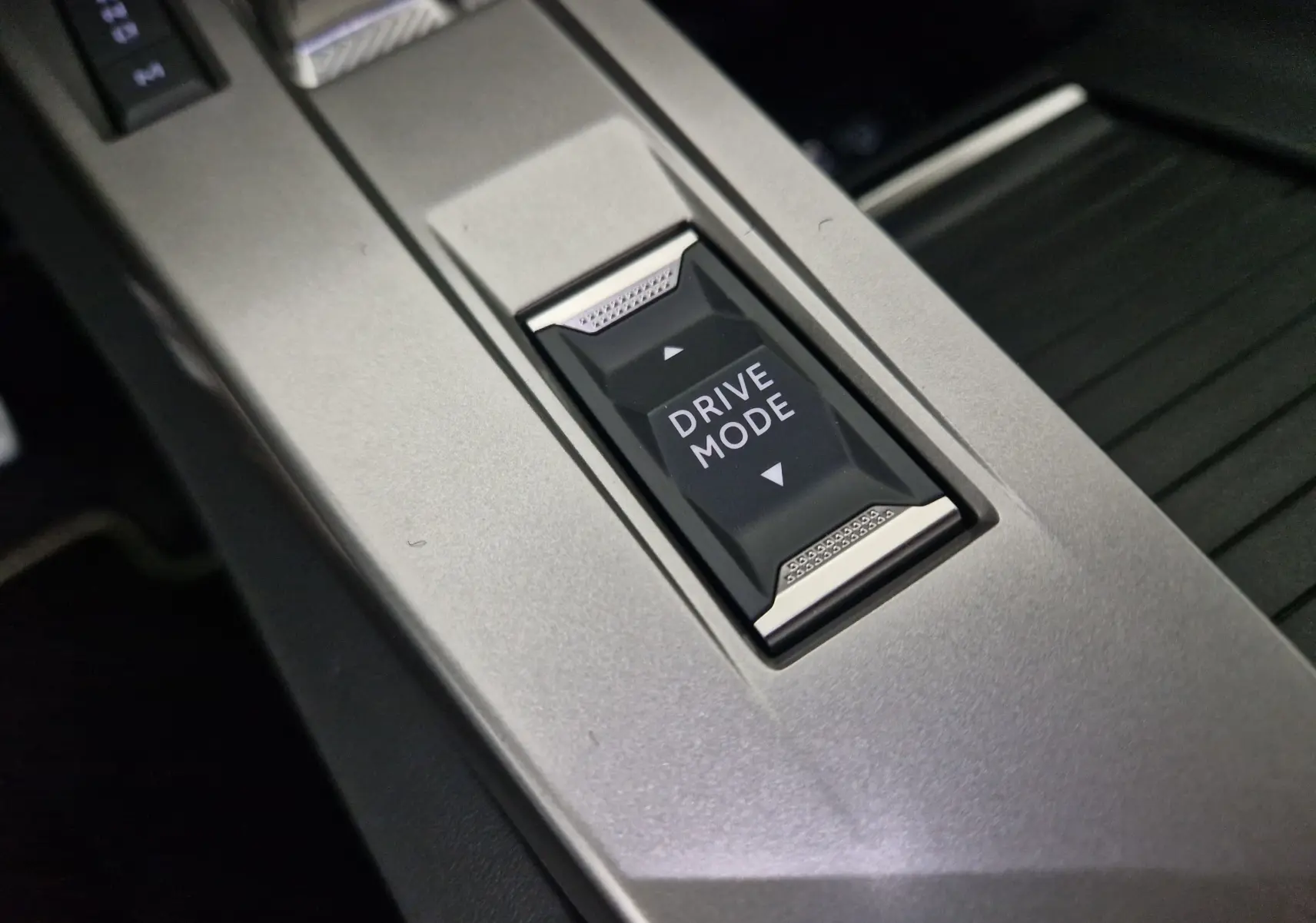 Gros plan sur le bouton Drive Mode noir encadré de métal dans la console centrale grise d'une Peugeot 308 blanche 2025.
