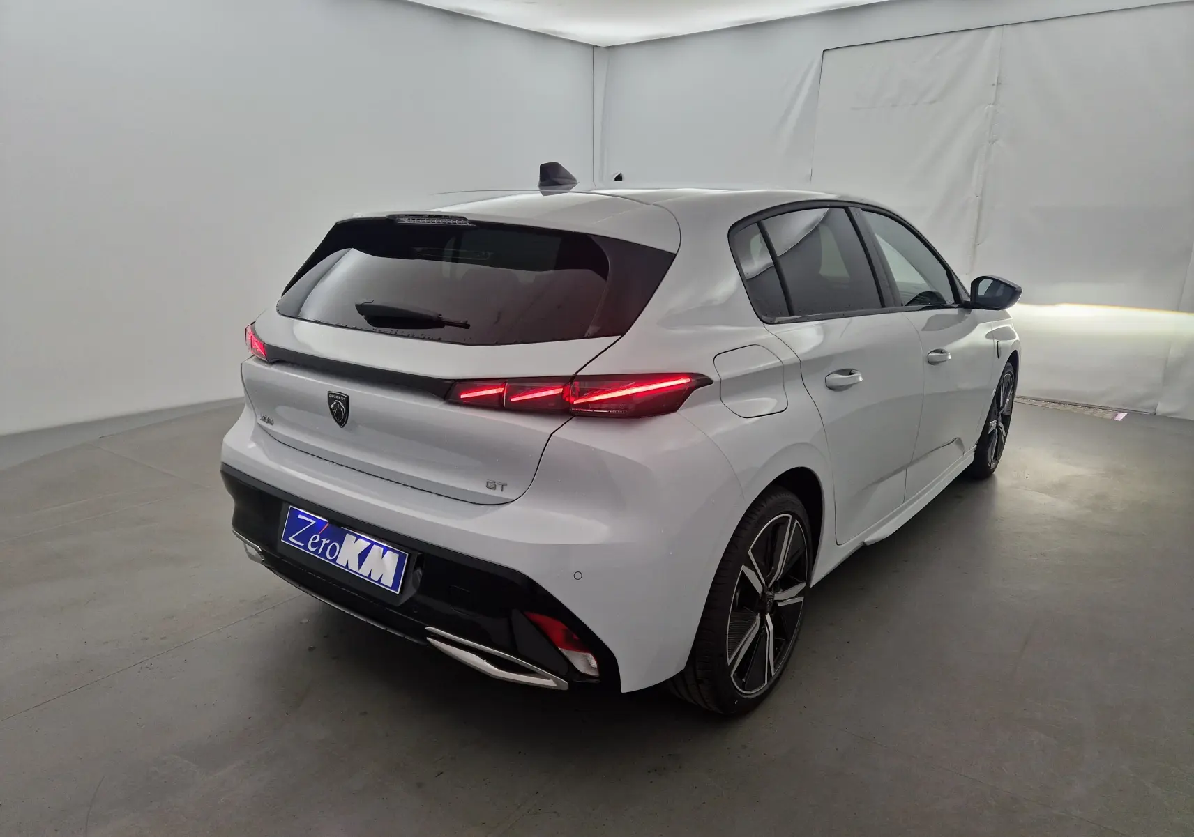 Peugeot 308 blanc Okenite vue 3/4 arrière droit, feux arrière allumés et jantes alliage distinctives.