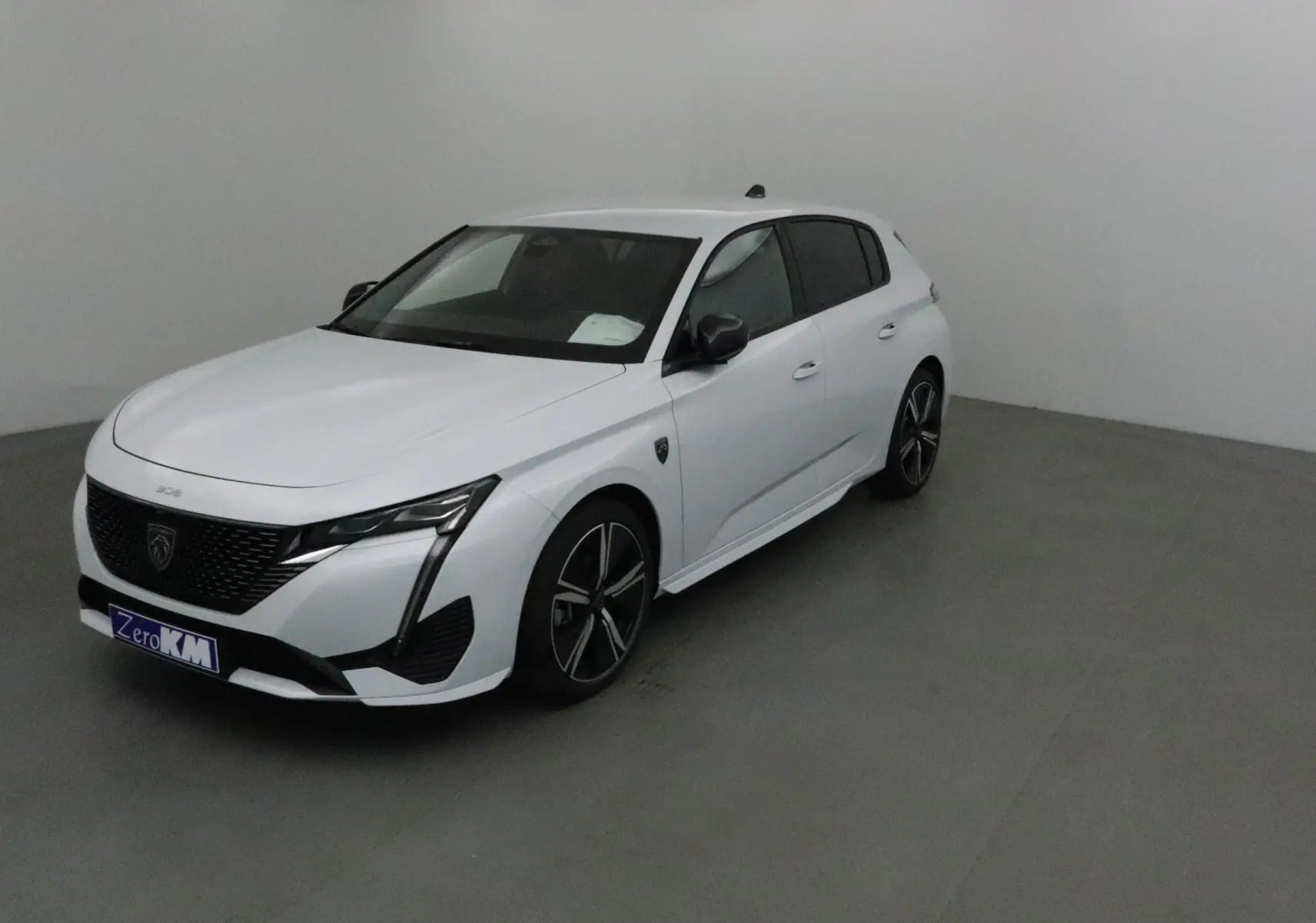 Peugeot 308 blanc Okenite vue 3/4 avant droit, avec jantes alliage noires et calandre noire distinctive.