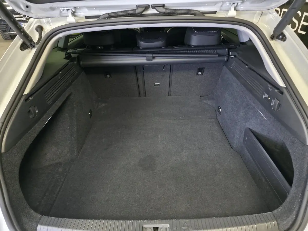 Coffre ouvert vu de l'arrière d'une Volkswagen Arteon Shooting Brake blanche, intérieur spacieux et tapis gris foncé.