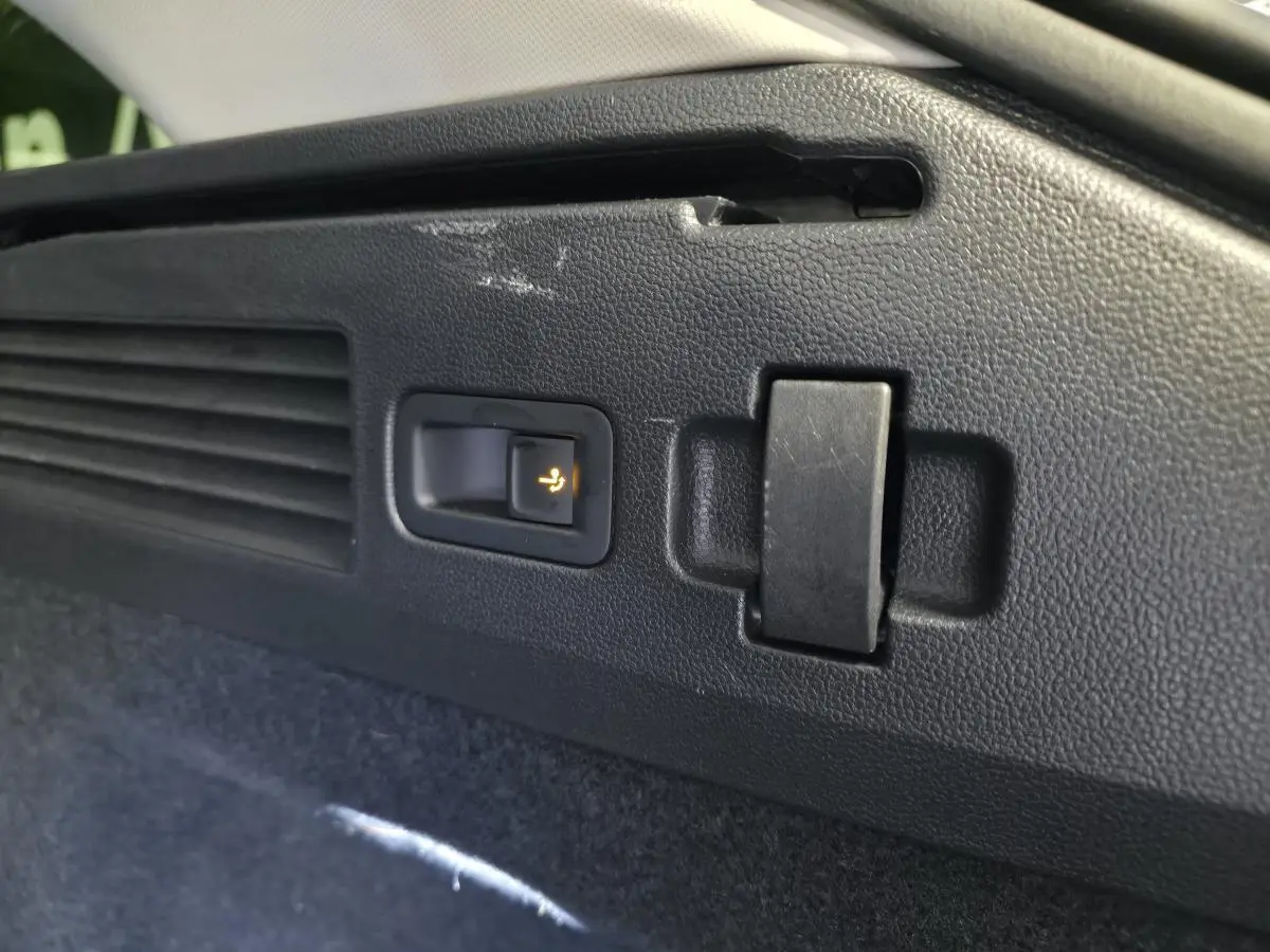 Détail du bouton d'ouverture électrique du dispositif d'attelage dans le coffre du Volkswagen Arteon blanc 2024.