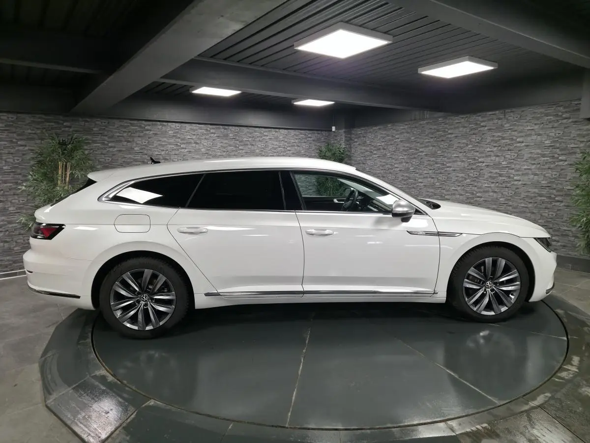 Profil côté gauche d'une Volkswagen Artéon Shooting Brake blanche nacrée avec jantes alliage 18 pouces dans un showroom.
