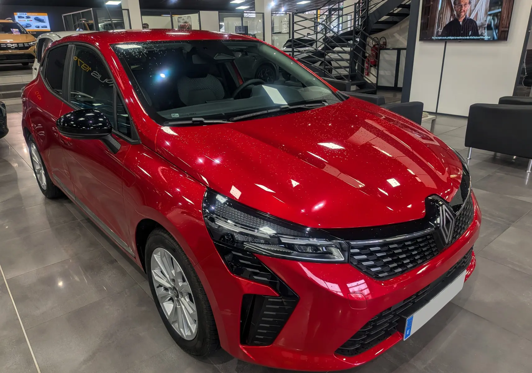 Renault Clio V rouge flamme vue 3/4 avant droit, avec calandre noire et feux LED modernes en showroom.