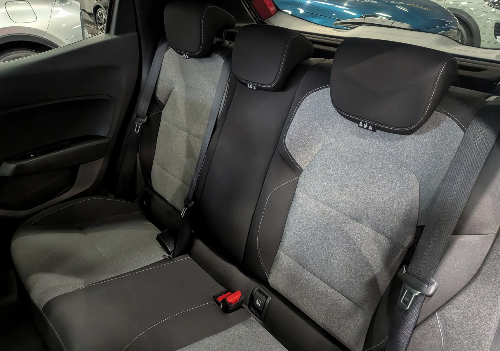 Vue intérieure des sièges arrière en tissu gris et noir de la Renault Clio V Rouge Flamme, avec ceintures de sécurité visibles.