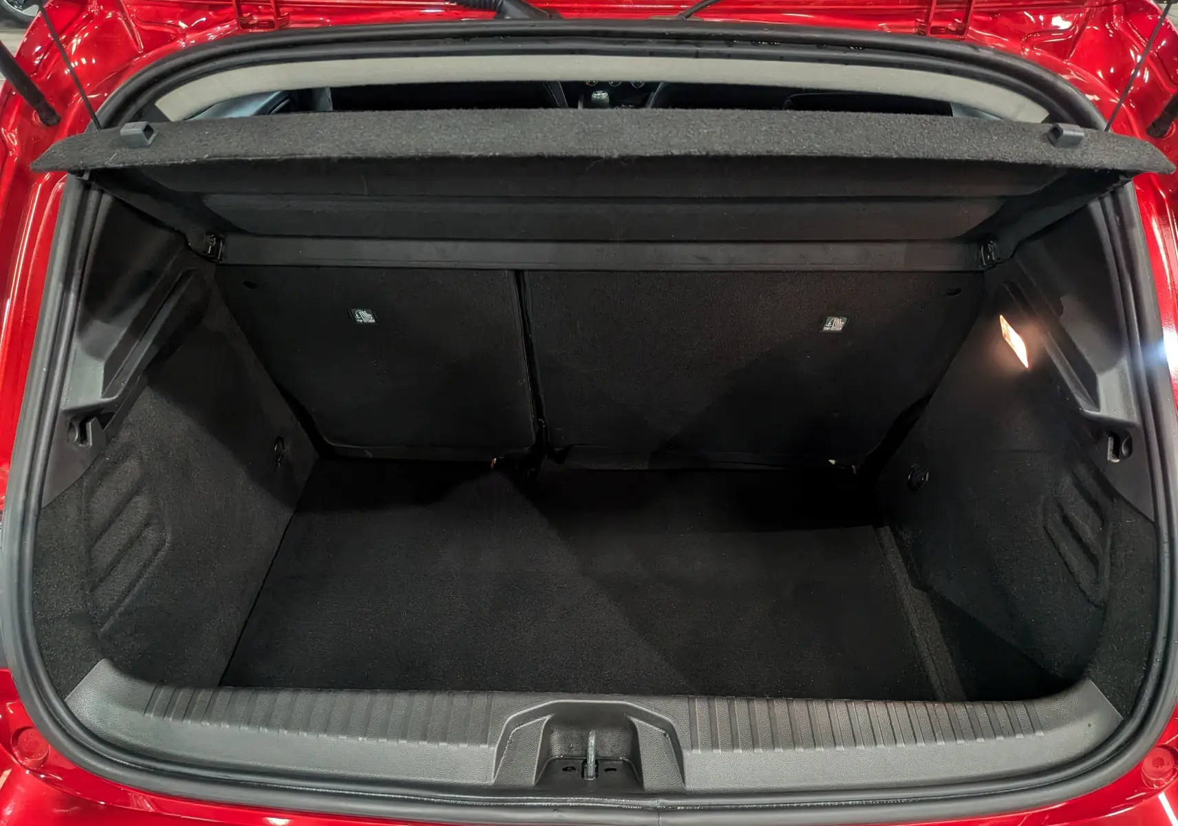 Coffre ouvert vu de l'arrière d'une Renault Clio V Rouge Flamme 2025, montrant l'espace de chargement vide et la lumière intérieure.