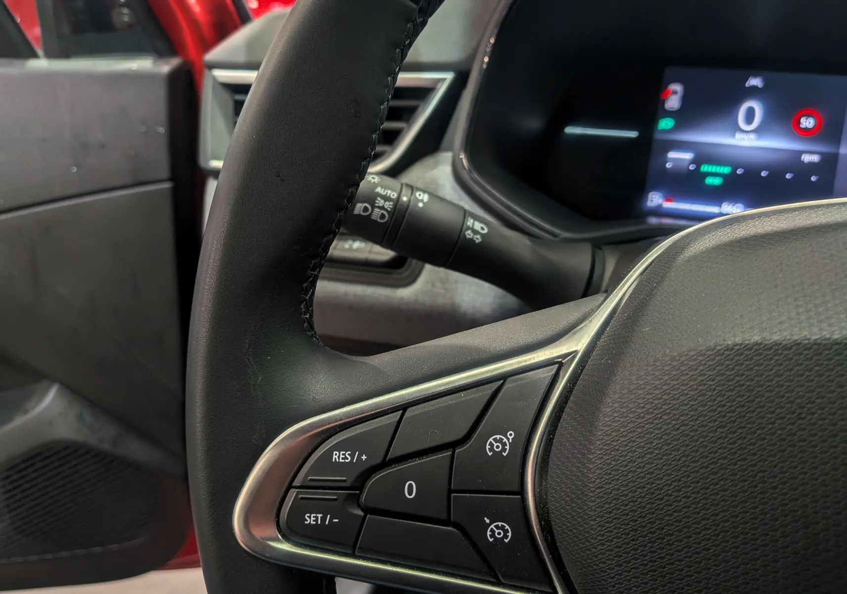 Gros plan sur le volant côté gauche de la Renault Clio V rouge Flamme, avec commandes de régulateur et tableau de bord numérique.
