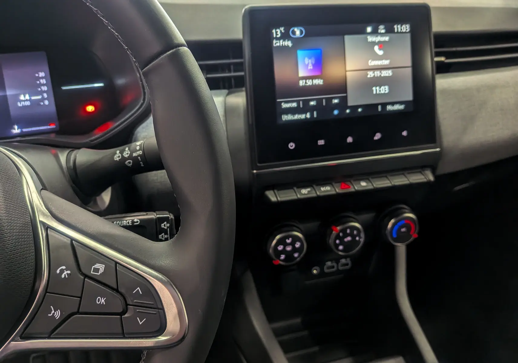 Vue rapprochée de l'intérieur de la Renault Clio V rouge, montrant le volant, l'écran tactile et les commandes de climatisation.