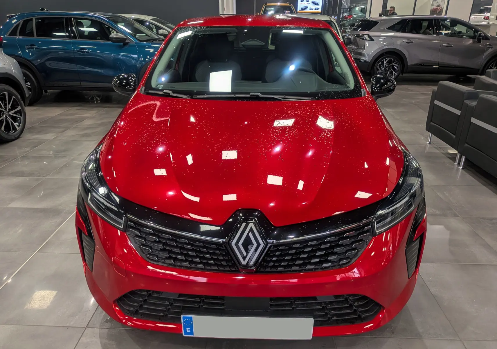 Vue frontale d'une Renault Clio V Rouge Flamme avec calandre noire et logo Renault bien visible en showroom.