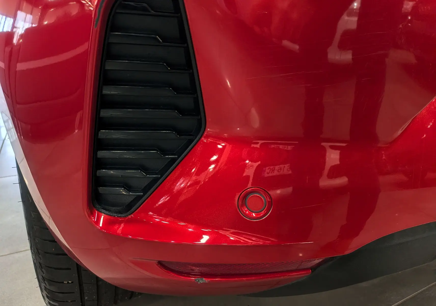 Gros plan sur le pare-chocs arrière droit rouge flamme d'une Renault Clio V avec capteur de recul et prise d'air noire.