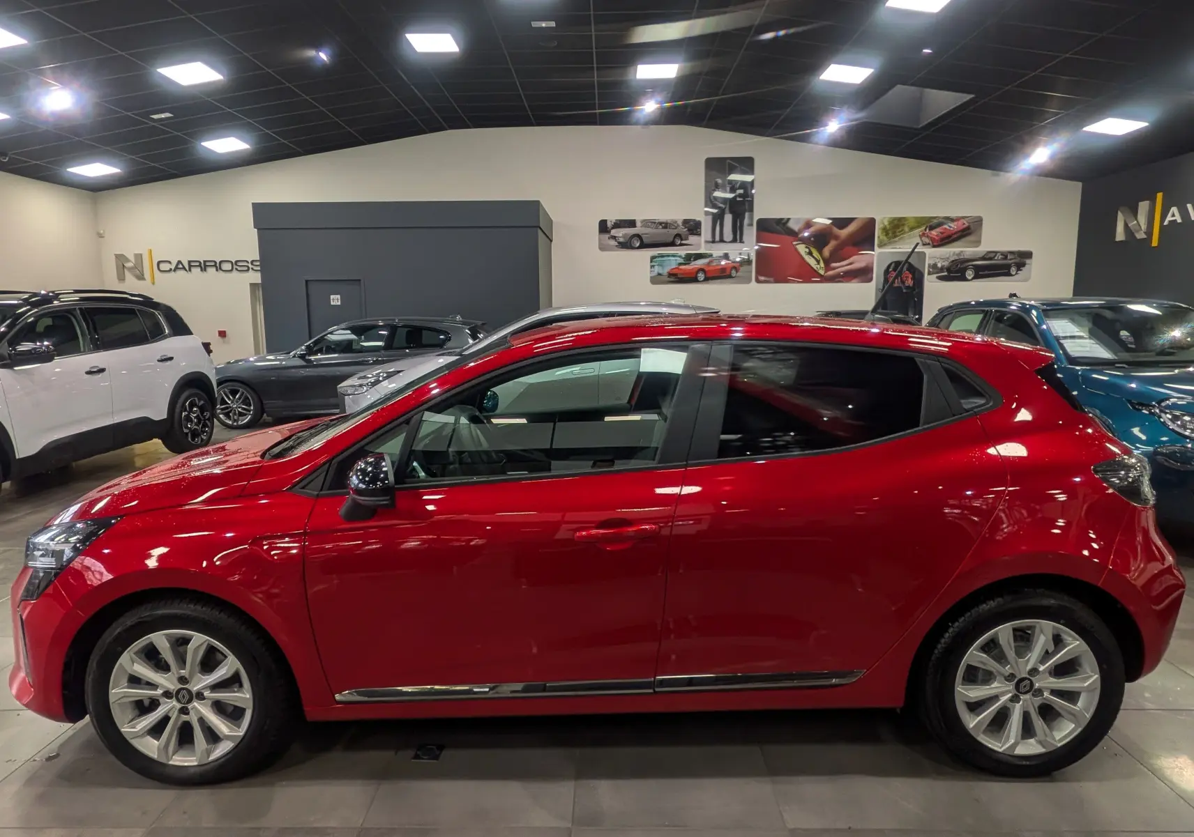 Profil côté gauche d'une Renault Clio V Rouge Flamme en intérieur, soulignant ses lignes dynamiques et jantes alliage.