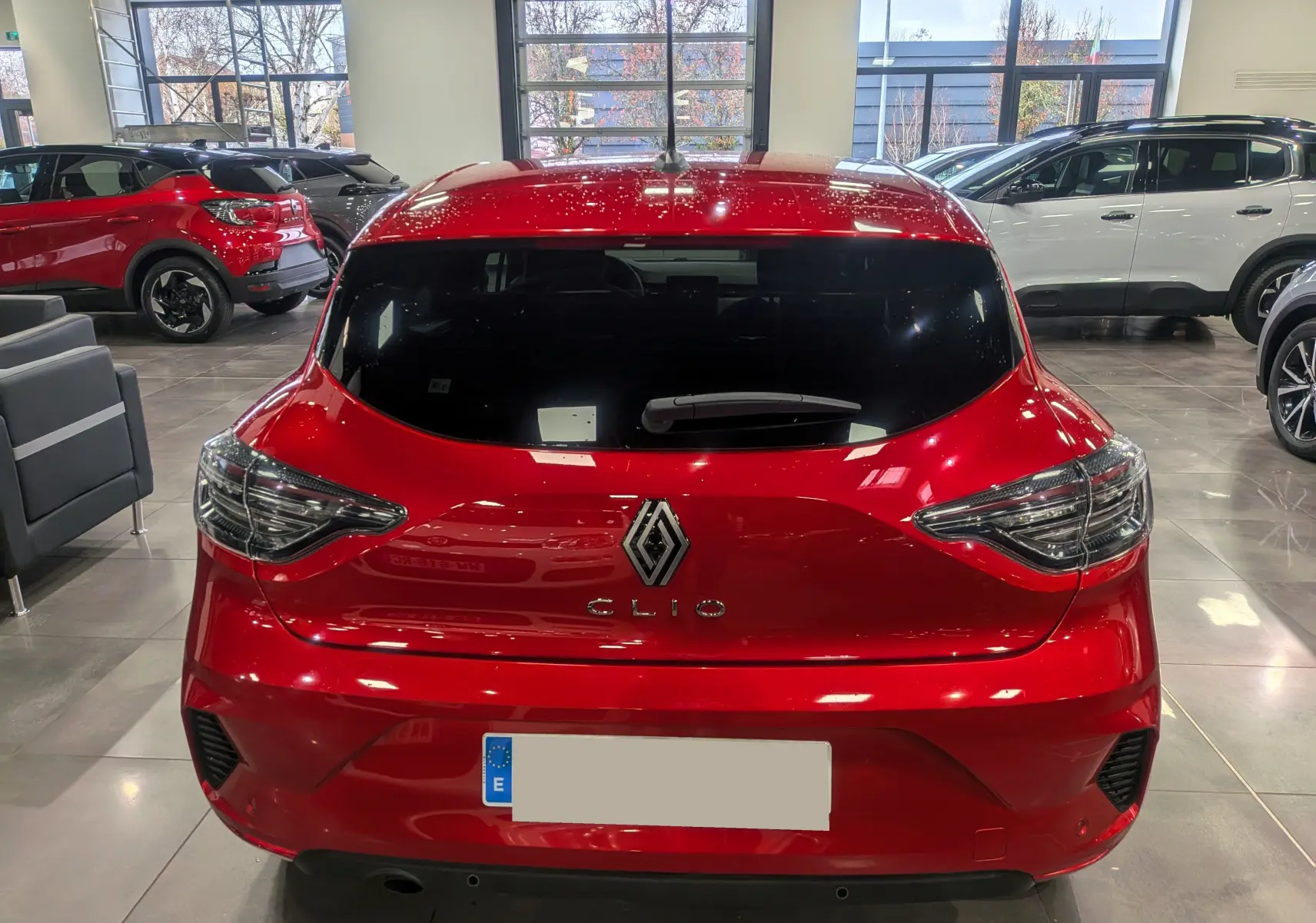 Vue arrière d'une Renault Clio V rouge flamme dans un showroom, avec feux arrière distinctifs et vitre teintée.