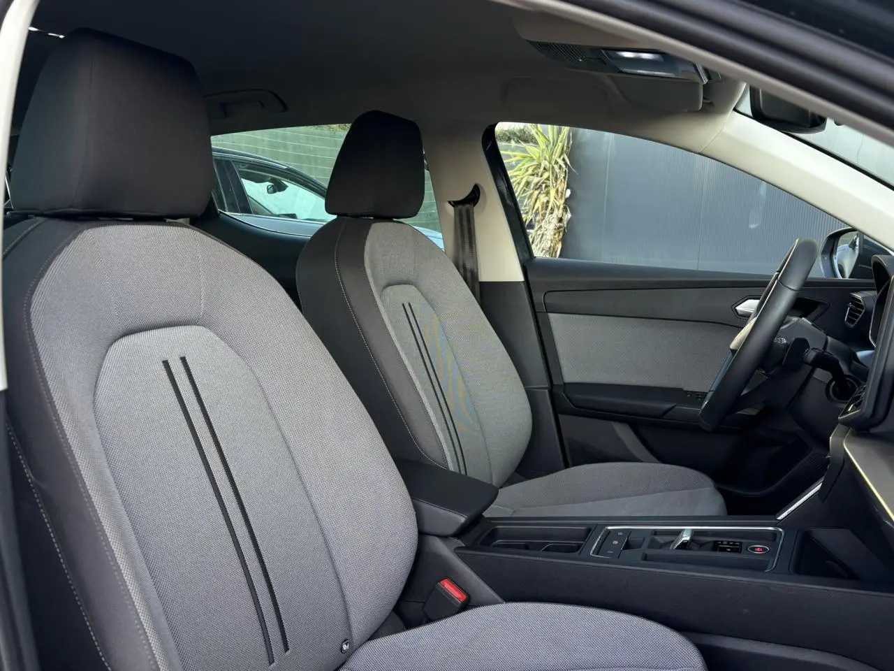 Vue intérieure côté conducteur du SEAT LEON 1.5 eTSI 115 DSG Style 2025, sièges tissu gris et accoudoir central noir.