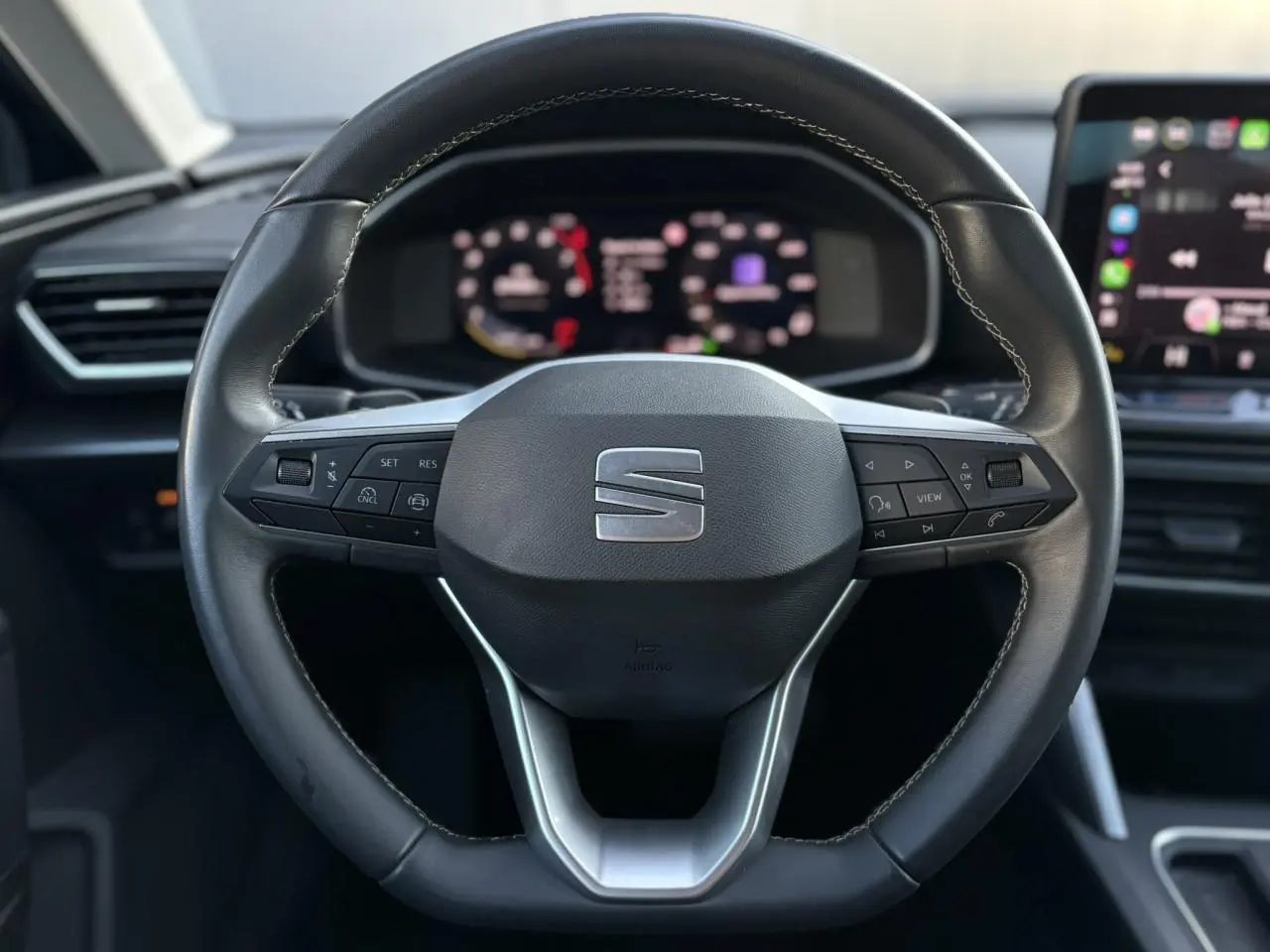 Vue frontale du volant cuir multifonction de la SEAT LEON 1.5 eTSI 115 DSG Style avec tableau de bord numérique flou en arrière-plan.