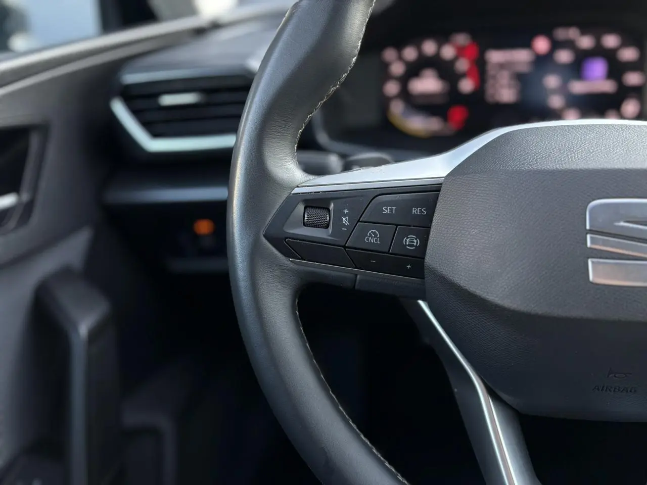 Gros plan sur le volant cuir multifonction côté gauche du SEAT LEON Bleu Fjord avec commandes de régulateur de vitesse.