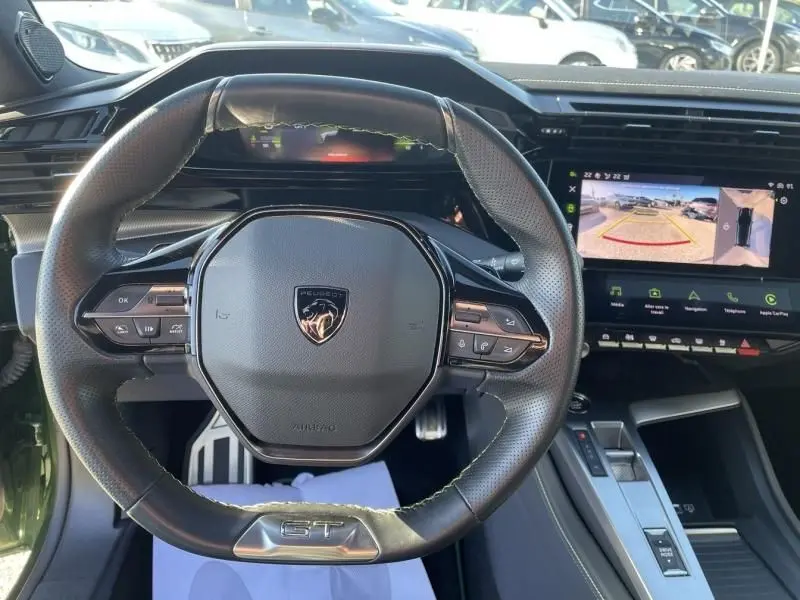 Vue rapprochée du volant GT de la Peugeot 308 1.5 HDI 130 vert olivine avec écran tactile et caméra de recul affichée.