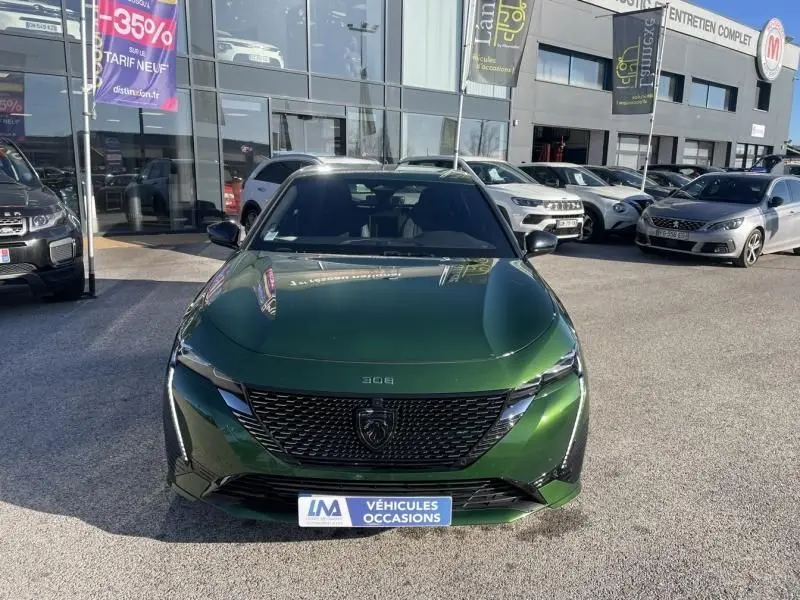 Peugeot 308 1.5 HDI 130 GT PACK vert olivine vue de face, calandre noire distinctive, en extérieur devant un showroom.
