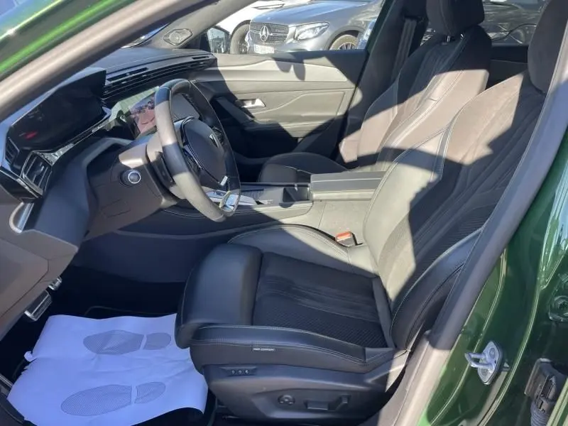 Vue intérieure côté conducteur de la Peugeot 308 1.5 HDI 130 GT PACK 2022, avec sièges noirs et portière vert olivine ouverte.
