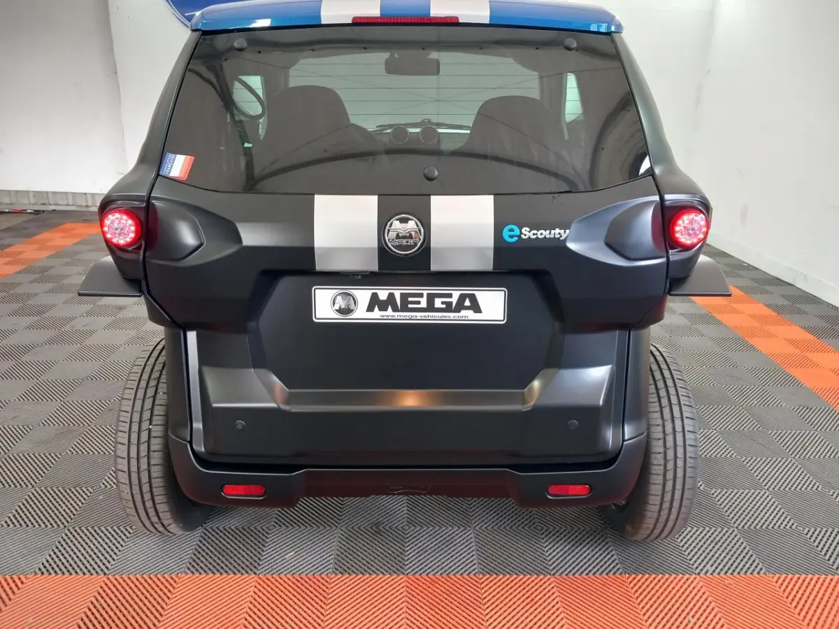 Vue arrière d'une Aixam MEGA E-Scouty Evo 2026 noire avec bandes grises et feux arrière allumés dans un garage.