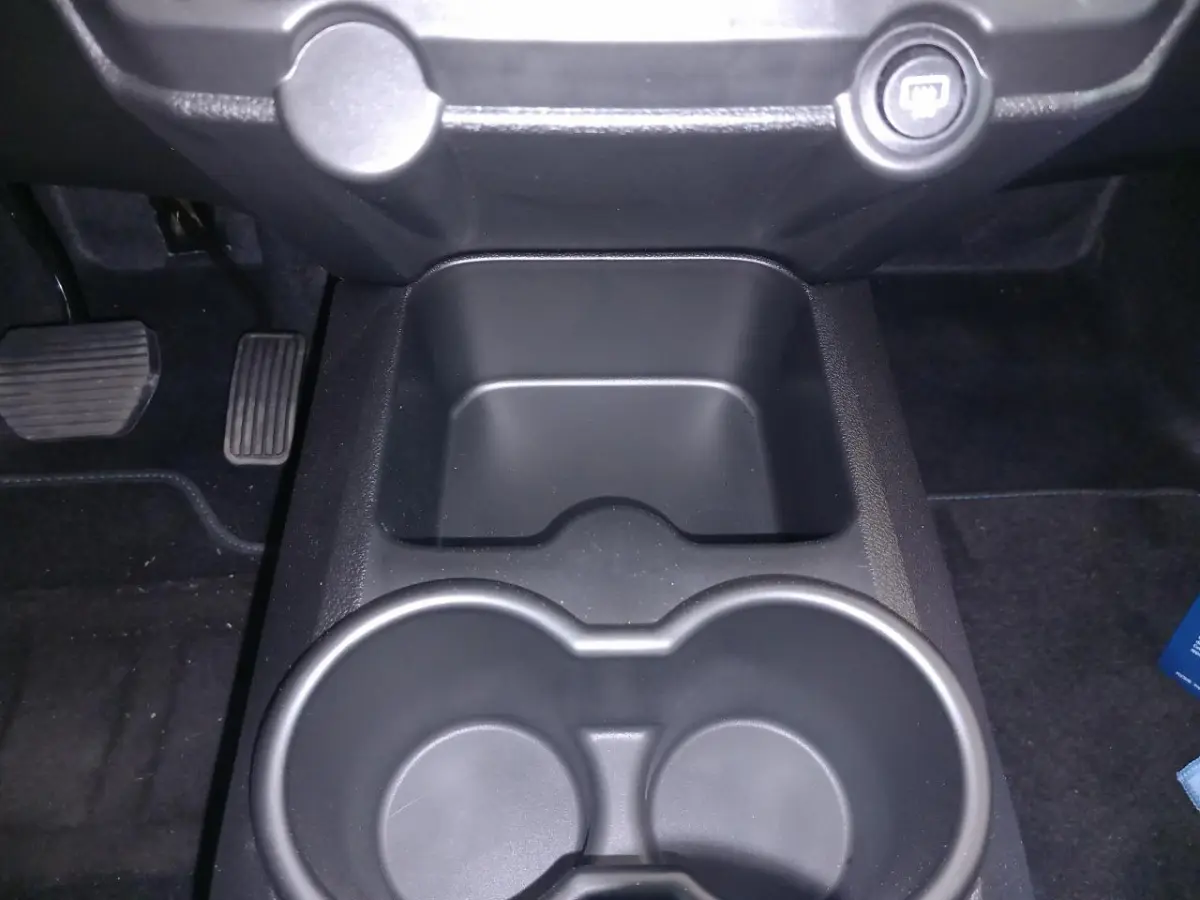 Gros plan intérieur sur la console centrale noire avec porte-gobelets et pédales au sol du côté conducteur.