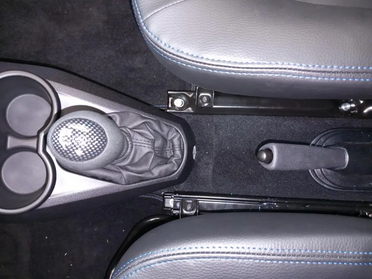 Vue intérieure centrée sur le levier de vitesse et frein à main entre deux sièges gris avec surpiqûres bleues.