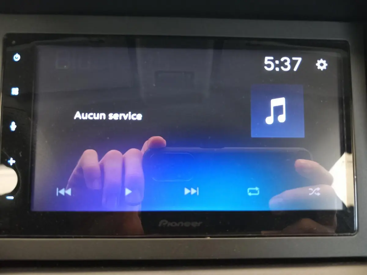 Écran tactile Pioneer du tableau de bord avec affichage musical et reflet des mains en gros plan.
