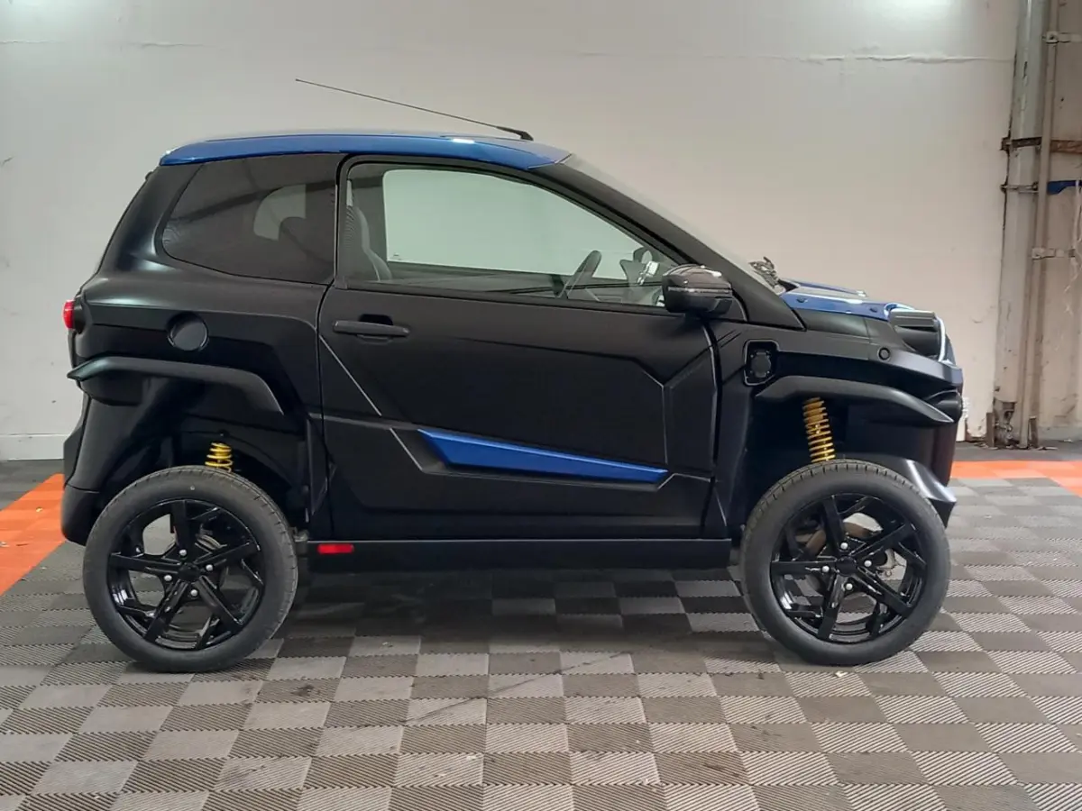 Vue de profil côté gauche d'une Aixam MEGA E-Scouty Evo 2026 bleu et noir avec suspensions jaunes et rétroviseur caméra.