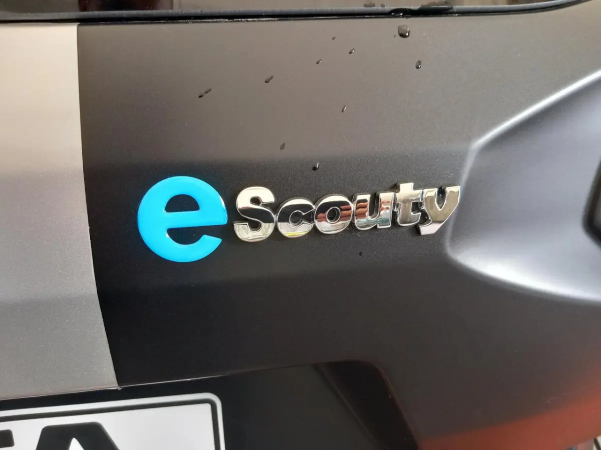 Gros plan sur le logo e-Scouty argenté et bleu sur la carrosserie noire d’un Aixam Mega électrique.