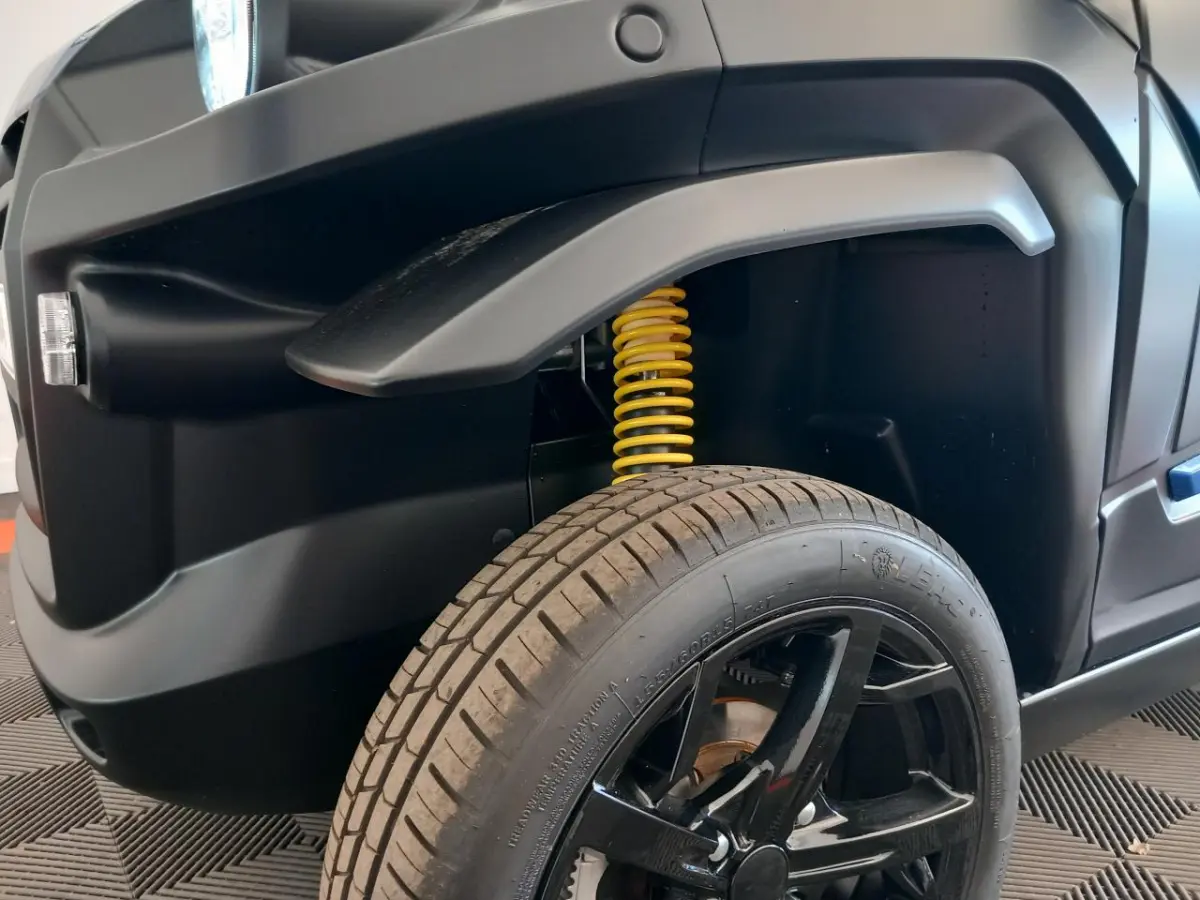 Gros plan sur l’avant droit bleu de l’AIXAM MEGA E-SCOUTY EVO 2026, mettant en valeur l’amortisseur jaune et la roue noire.