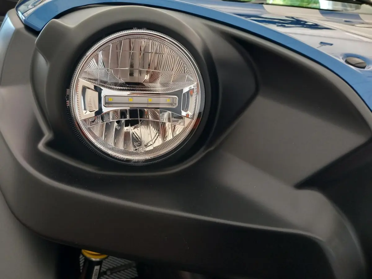 Gros plan sur le phare avant droit de l'AIXAM MEGA E-SCOUTY EVO bleu, soulignant le contour noir mat du pare-chocs.