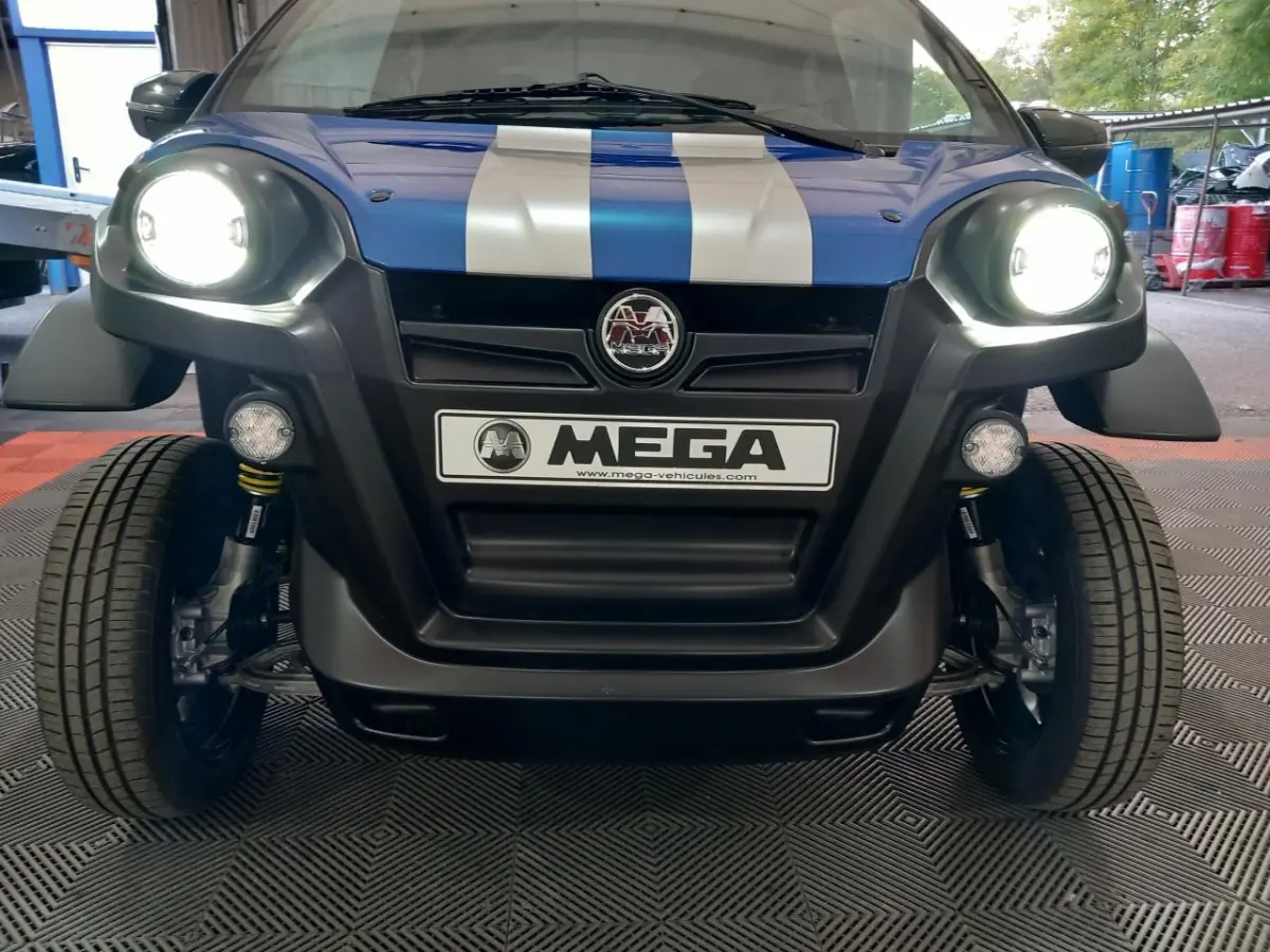 Vue frontale d'une Aixam MEGA E-Scouty Evo bleue avec phares allumés et bandes blanches sur le capot.