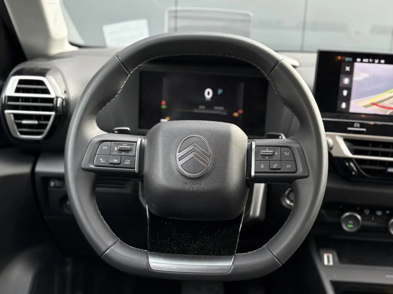 Vue rapprochée du volant cuir noir de la Citroën C4 2025 avec commandes intégrées et tableau de bord numérique en arrière-plan.