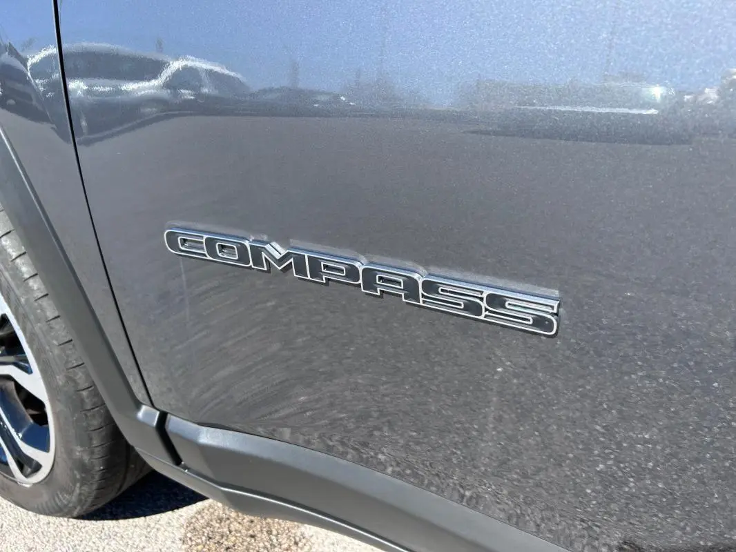 Gros plan sur l’inscription Compass côté gauche d’un Jeep Compass gris métallisé avec jante alliage visible.