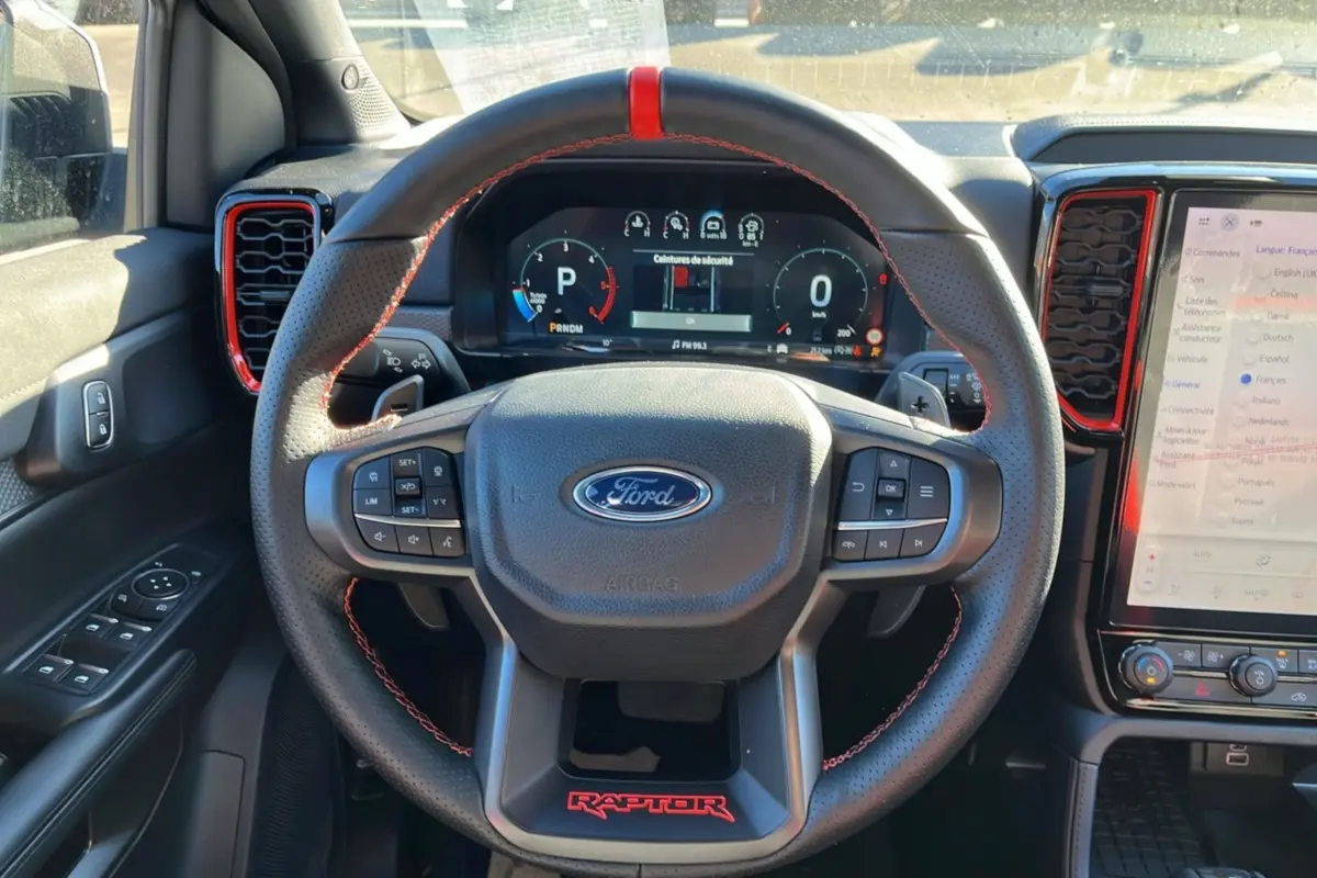 Vue intérieure centrée sur le volant cuir noir avec surpiqûres rouges et tableau de bord digital du Ford Ranger Raptor 2026.