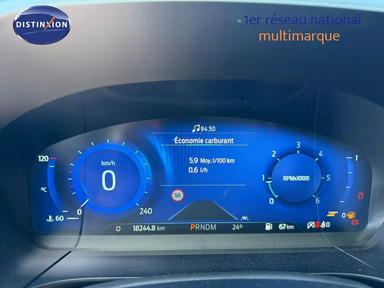 Vue rapprochée du tableau de bord numérique bleu du Ford Kuga 2024, affichant vitesse, régime et consommation.